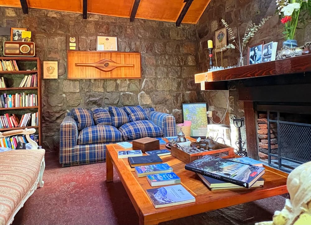 El salón de la chimenea, con muros de piedra, libros y un sofá a cuadros